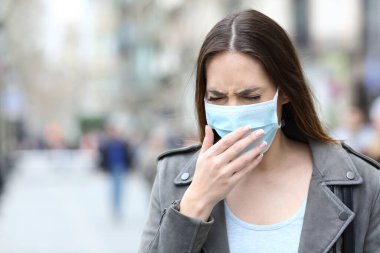 Portrait of a sick woman with protective medical mask coughing on city street