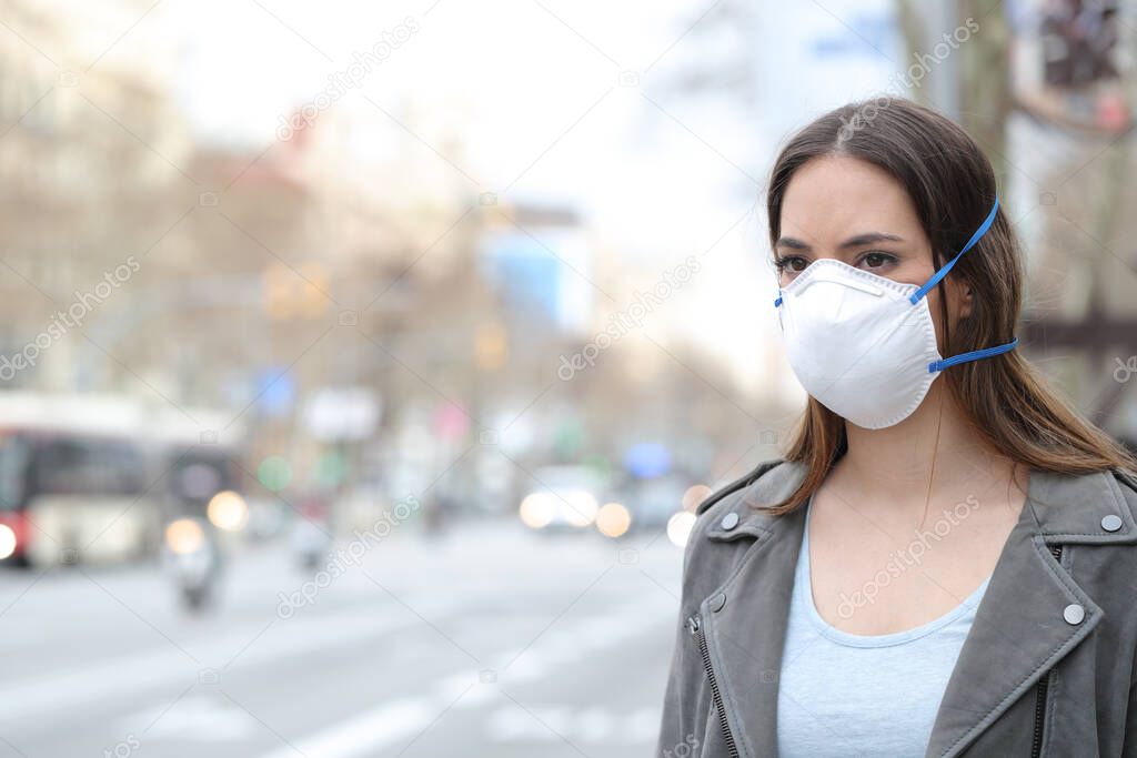 Serious woman wearing protective mask avoiding pollution looking at city road 