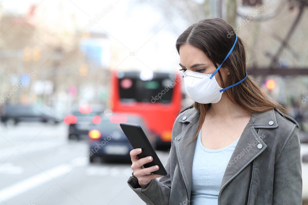 Woman with protective mask avoiding pollution using smart phone with city traffic background
