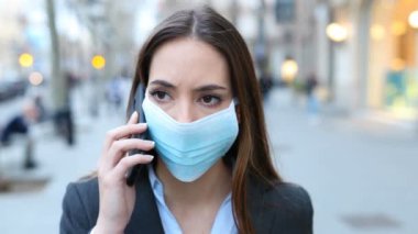 Serious executive wearing mask talking on mobile phone walking in the street