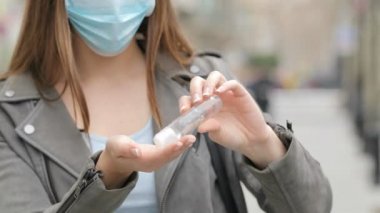 Young woman with protective mask cleaning hands with sanitizer in the street
