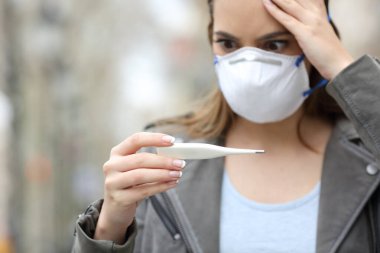 Koruyucu maskeli endişeli kızın yakın çekim sonucu sokakta bir termometre.