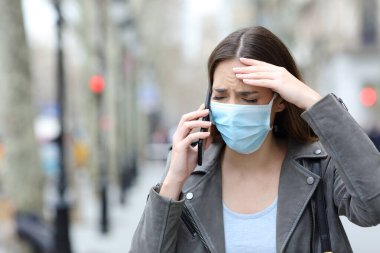 Korumacı maskeli hasta bir kadının caddede akıllı telefondan araması ön planda.