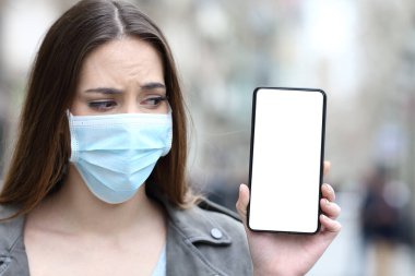 Koruyucu maskeli korkmuş bir kızın portresi. Salgını önlüyor. Boş akıllı telefon ekranına bakıyor. 