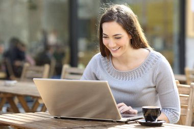 Kahve dükkanının terasında dizüstü bilgisayar kullanan mutlu genç bir kadın.