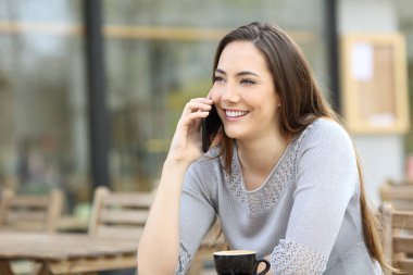 Kafenin terasında akıllı telefonda konuşan mutlu genç bir kadın.