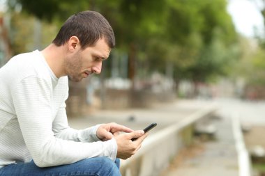 Ciddi yetişkin bir adamın parkta tek başına akıllı telefon kullanması.