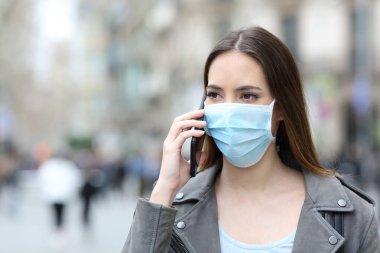 Şehir caddesinde akıllı telefondan konuşan koruyucu maskeli bir kadının portresi.