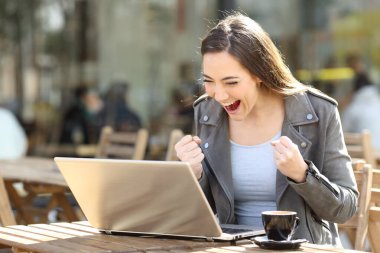 Bir kafenin terasında oturan dizüstü bilgisayarda iyi haber okuyan heyecanlı kadın