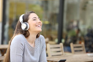 Mutlu kadın temiz hava soluyor. Kafe terasında kulaklıkla müzik dinliyor.