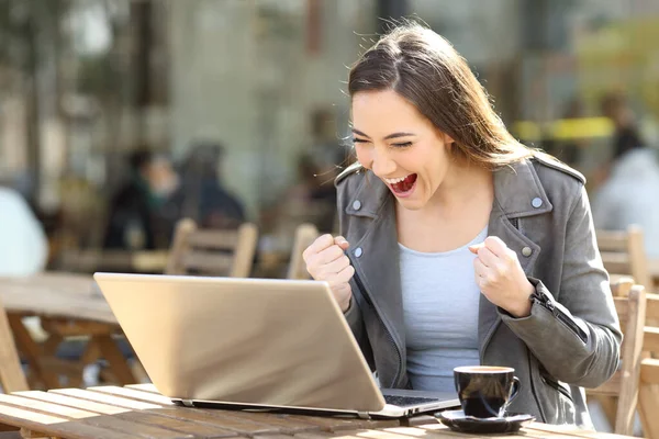 兴奋的女人阅读好消息的笔记本电脑坐在咖啡店露台 — 图库照片