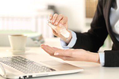 Ofisteki bir masada oturan iş kadını dezenfektanla ellerini temizliyor.