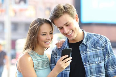 Mutlu genç çift sokakta duran akıllı telefondan içeriği okuyor.
