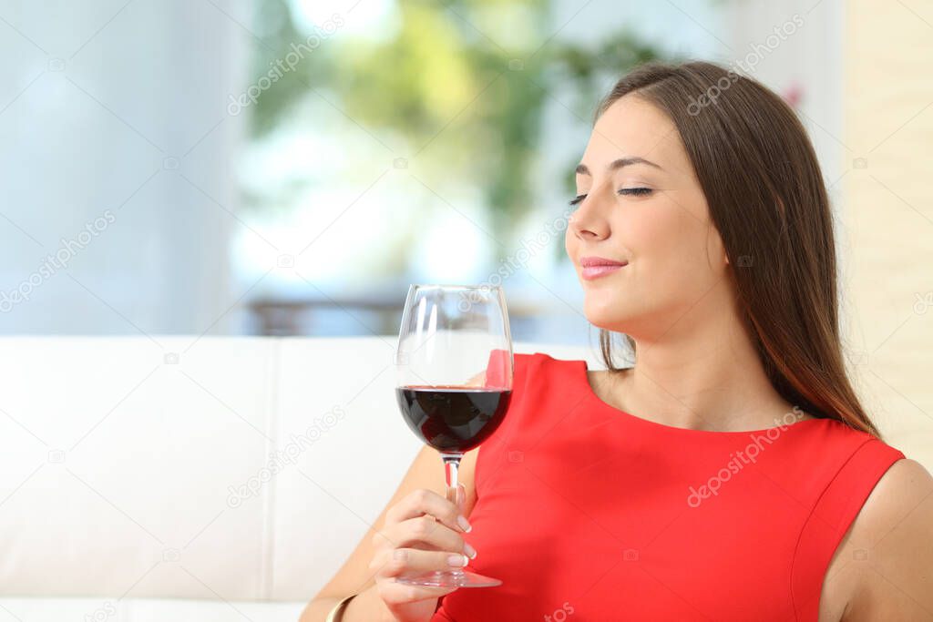 Satisfied woman smelling a red wine glass sitting on a couch at home