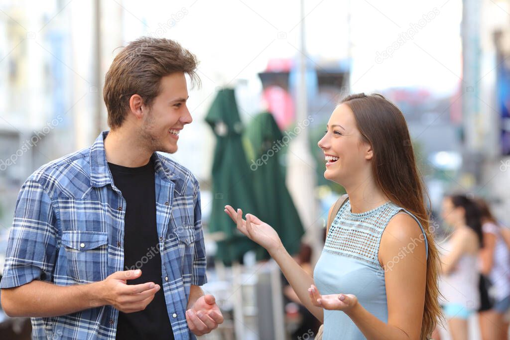 Two happy friends meeting and talking in the street on a city