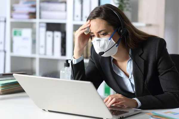 Worried telemarketer with protective mask looking at bad news on laptop in the office