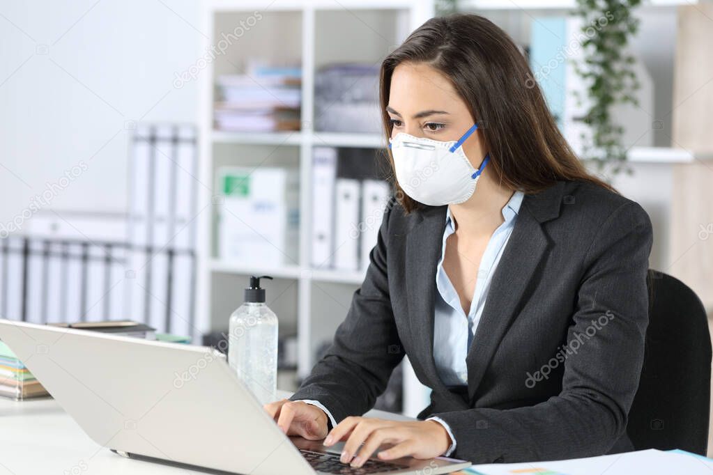 Serious executive woman wearing mask working on laptop on a desk at office