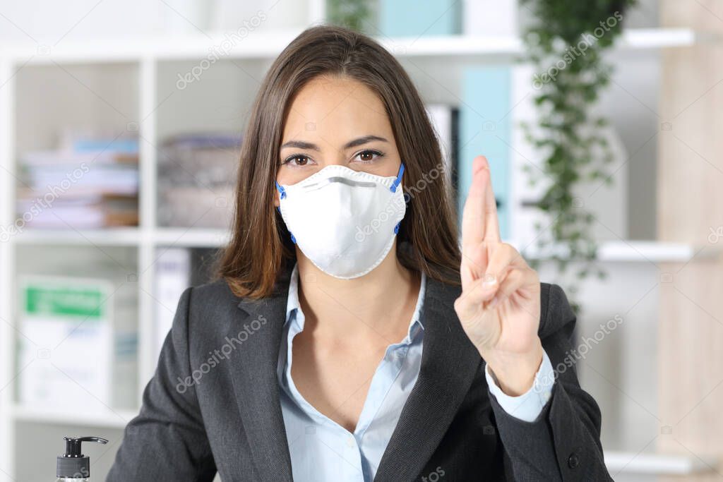 Front view of executive woman with protective mask crossing fingers looking at camera at office