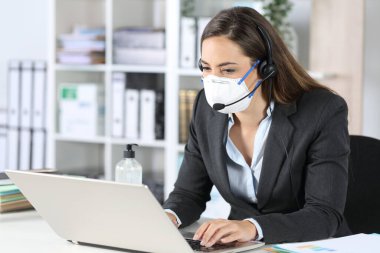 Telemarketer woman working on laptop avoiding covid-19 with mask sitting on a desk at office clipart