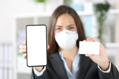 Yönetici kadının ön görüntüsünde boş akıllı telefon ve kredi kartı modeli görünüyor. Ofiste COVid-19 'dan kaçınıyor.