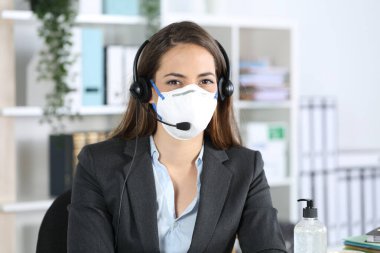 Happy telemarketer woman posing looking at camera avoiding covid-19 with mask sitting at the office clipart
