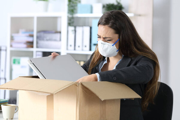 Sad fired executive woman with protective mask crying packing her stuff on a box at the office