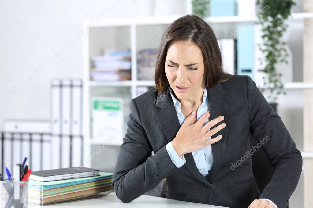 Sick executive woman suffocating holding chest sitting on a desk at office