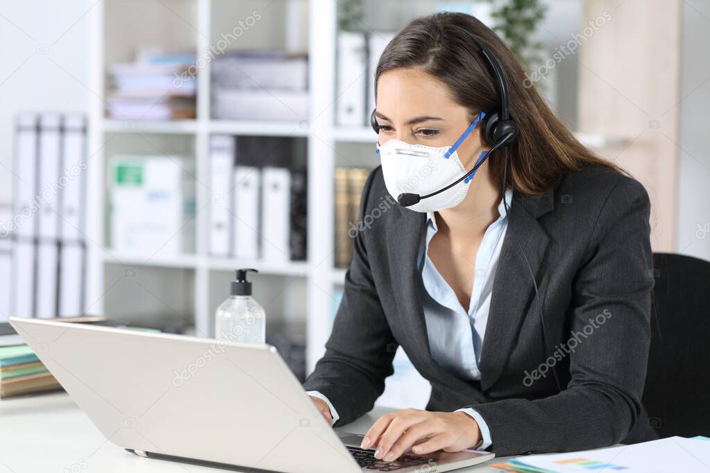Telemarketer woman working on laptop avoiding covid-19 with mask sitting on a desk at office
