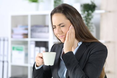 Ofiste elinde kahve fincanı tutan, diş ağrısı çeken bir kadın.