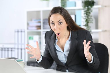 Ofisteki masasında oturan hayret verici yönetici kadın kameraya şaşkın bakıyor.