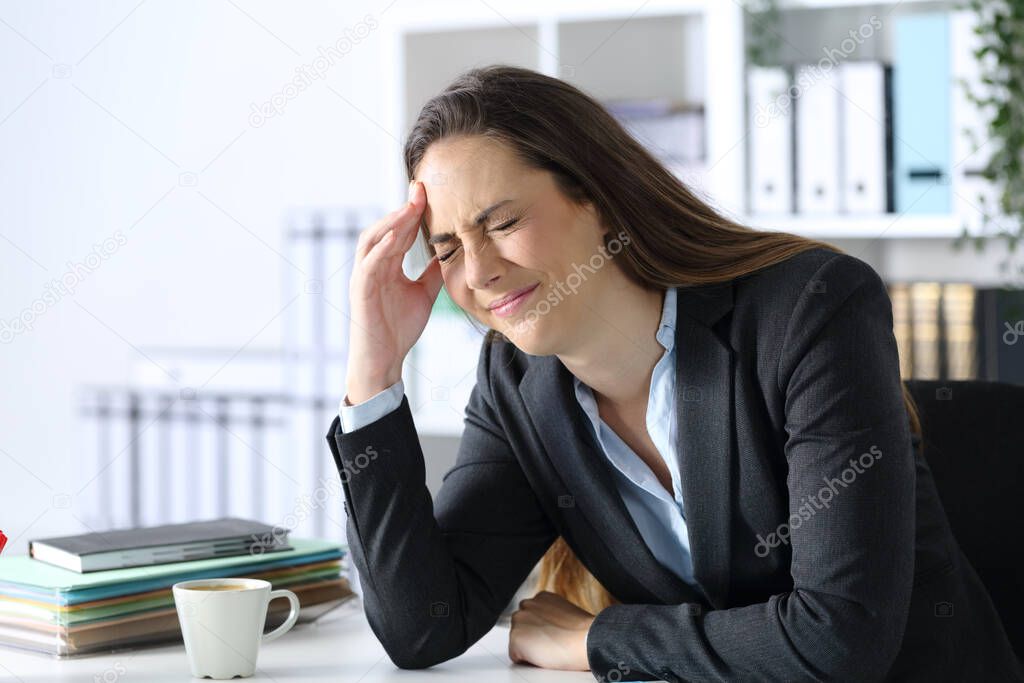 Executive in pain suffering headache touching head side sitting at office desk