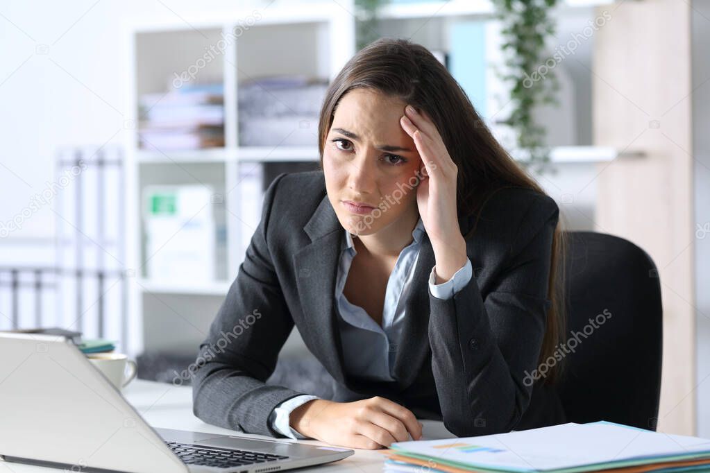Sad executive woman compaining looking at camera sitting on her desk at office