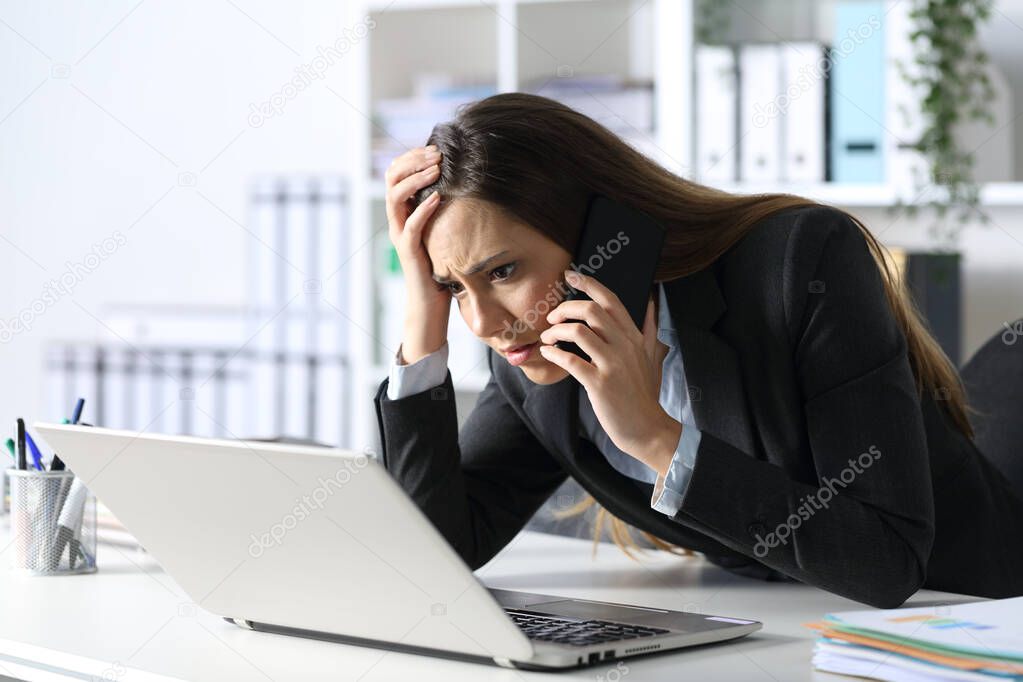 Sad executive woman calling on smart phone reading on laptop sitting on her desk at office