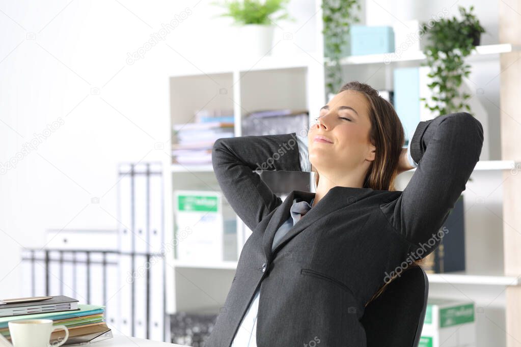 Satisfied executive woman relaxing sitting on a desk resting head on arms at the office