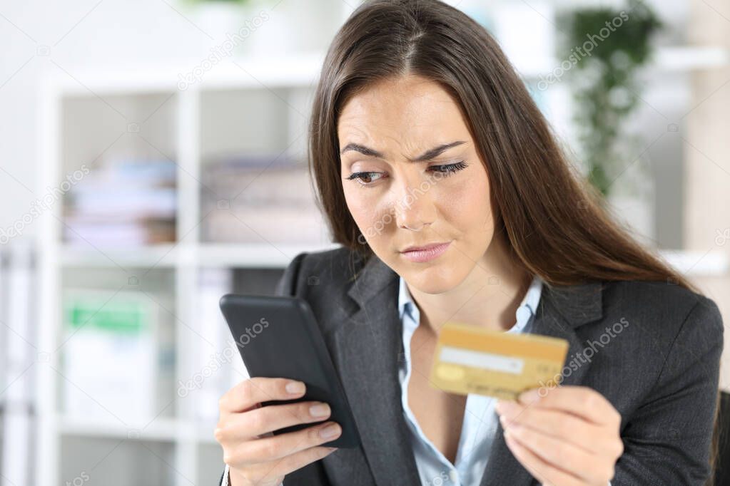 Suspicious executive woman pays with credit card on smart phone sitting at the office