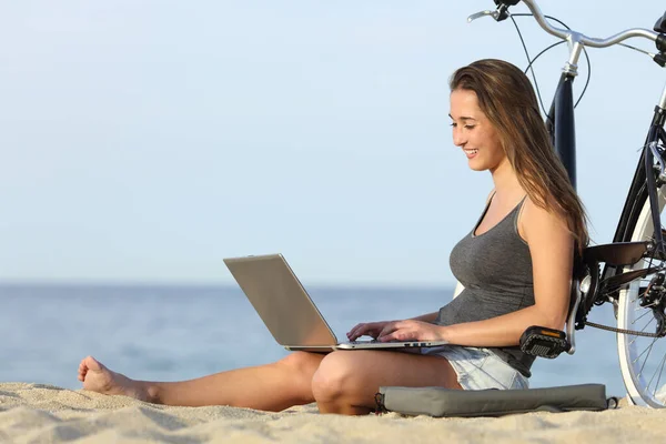 骑自行车的快乐女孩坐在沙滩上的笔记本电脑上 — 图库照片
