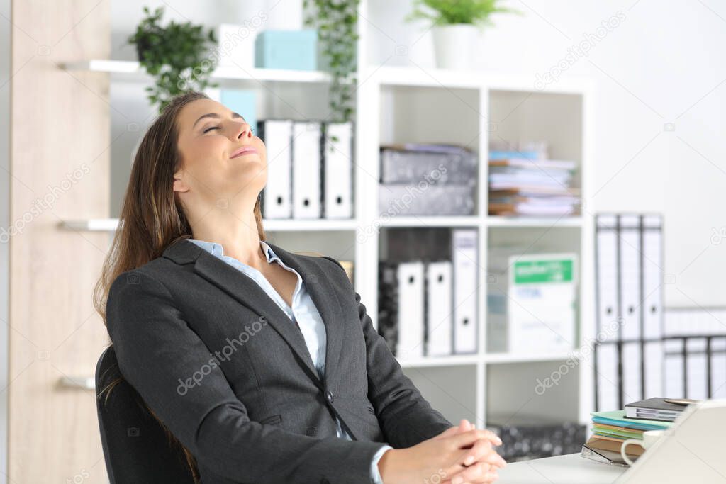 Happy executive woman breathing fresh air sitting on a desk at the office