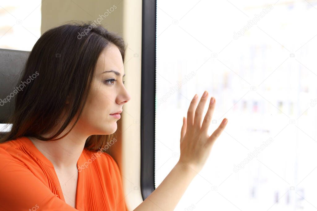 Pensive sad woman looking through window with hand on glass sitting on a train