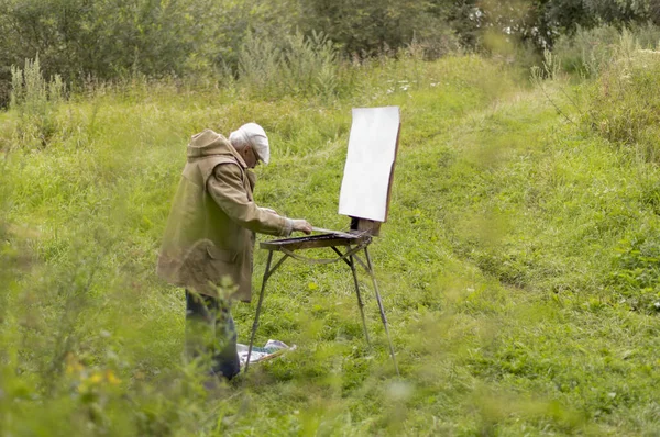 Un anciano está interesado en pintar con pinturas al óleo. Dibujar un paisaje natural — Foto de Stock