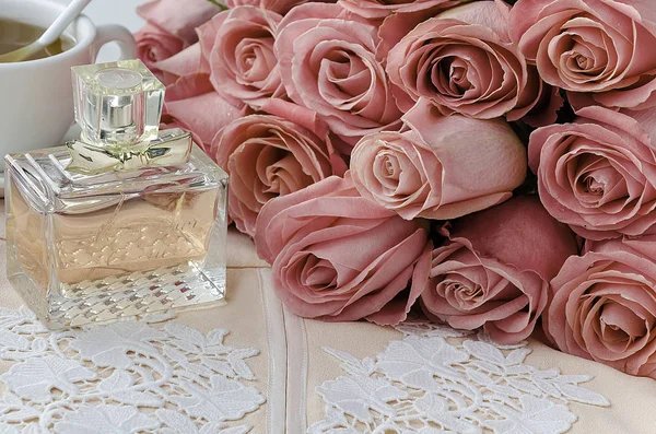 Fles parfum, geborduurde ontwerper rok, kopje thee en bos van rozen — Stockfoto