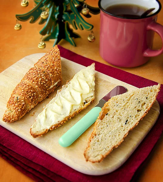 Sesame olive wholegrain croissant with soft cheese and tea served on the wooden board and linen cloth with Christmas tree on the background