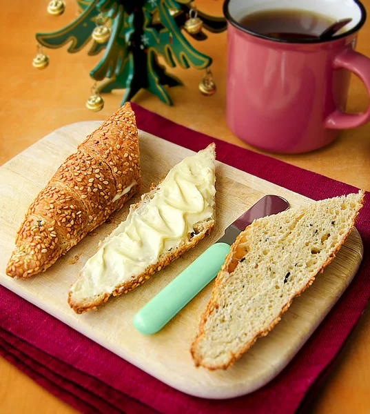 Sesam-Oliven-Vollkorncroissant mit Weichkäse und Tee auf dem Holzbrett und Leinentuch mit Weihnachtsbaum im Hintergrund — Stockfoto