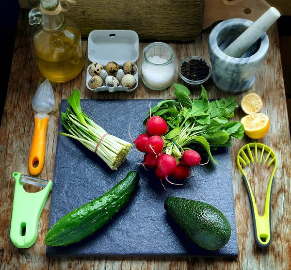 Spring salad with radishes, ramson, avocado, cucumber and quail eggs arranged on the black tile on the vintage wooden table. — Stock Photo, Image