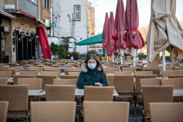 在德国科隆 严重的年轻女性带着防护面罩坐在空旷的咖啡厅阳台上 — 图库照片