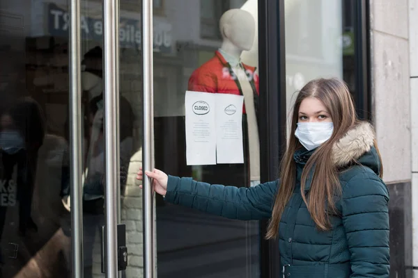 コロナウイルスのパンデミックの間閉鎖された店を見て保護医療マスクを身に着けている若い女性 ロイヤリティフリーのストック画像