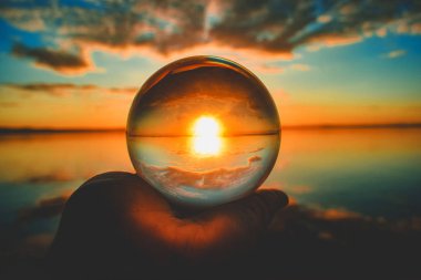 Günbatımının arka planda bulanık bulutlarla çekilmiş yaratıcı bir kristal mercek küresi fotoğrafı.