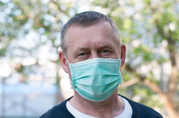 mid age european man with surgery face mask on backyard background in sunny spring day