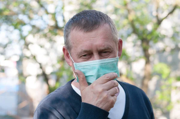 mid age european man with surgery face mask on backyard background in sunny spring day