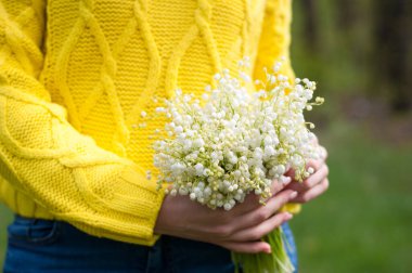 Sarı kazaklı kız iki eliyle buket tutuyor.