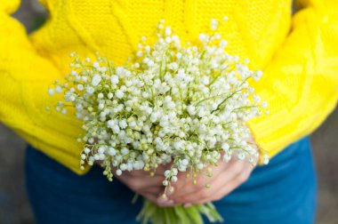Kız vadideki zambak buketini iki eliyle tutuyor.